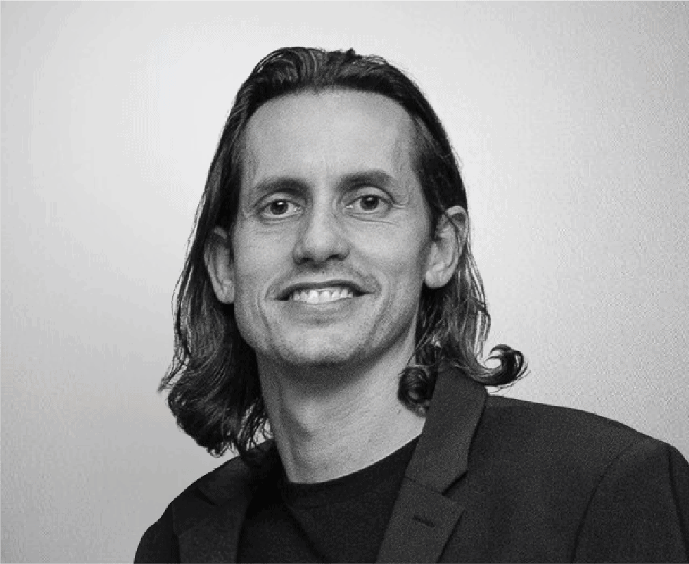 Portrait of a smiling man with long hair in black and white, wearing a blazer and casual shirt, suitable for professional or creative industry profiles.