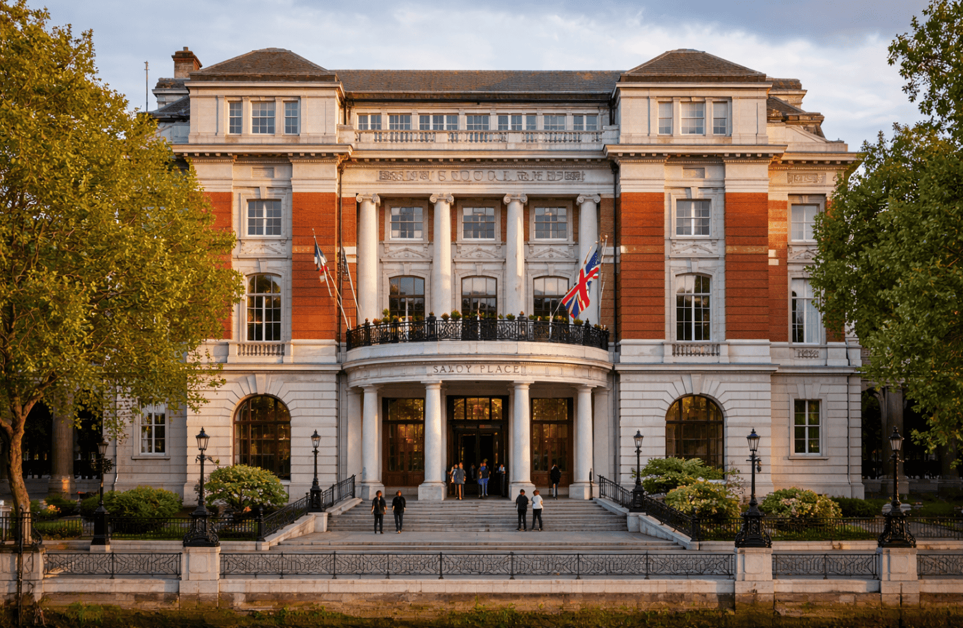 Elegant historic building with British flags, surrounded by lush trees, featuring classical architecture with columns and large windows, set against a clear sky.