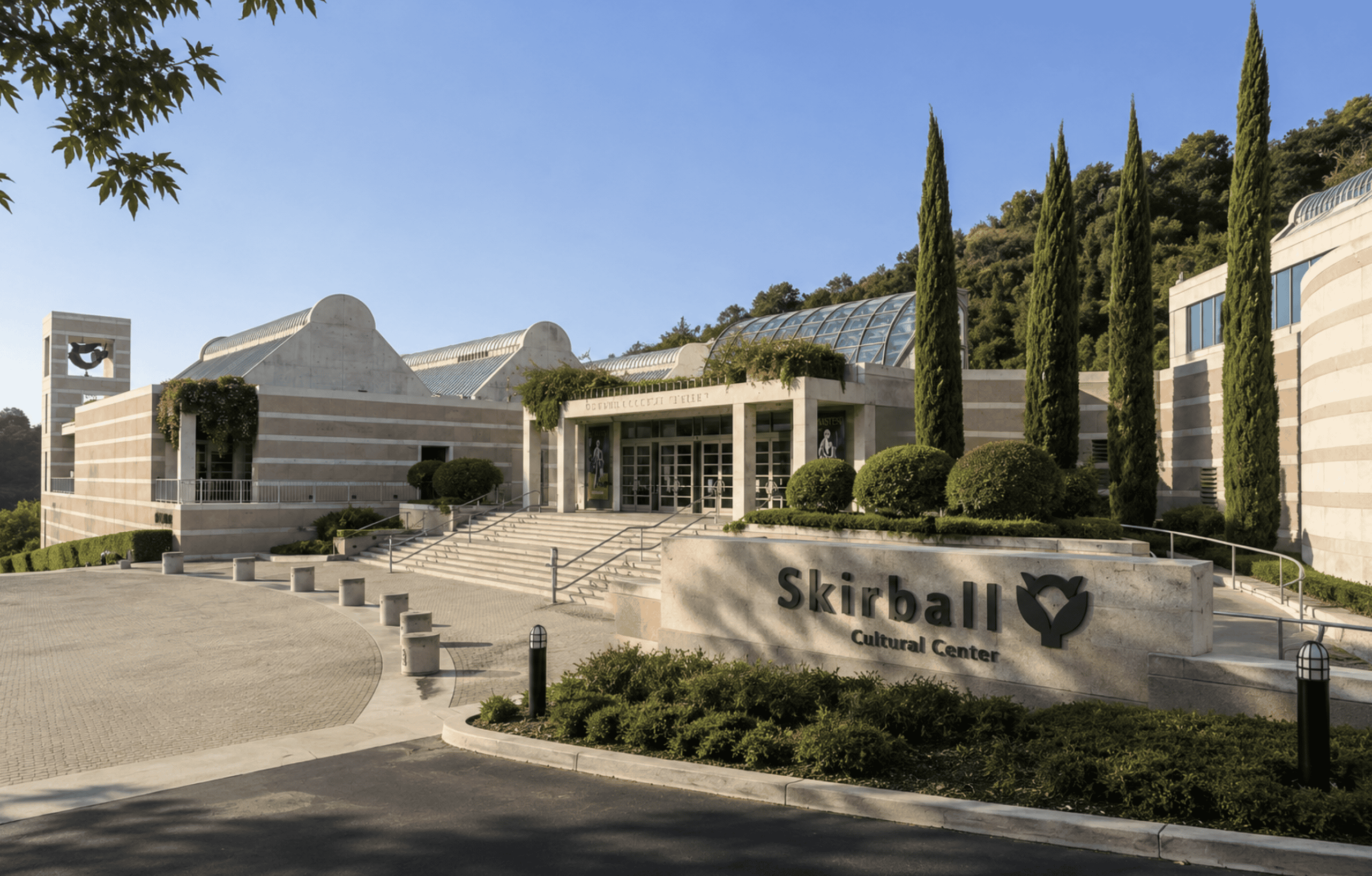 Exterior view of SkiBall Cultural Center with landscaped gardens and tall cypress trees during daytime.