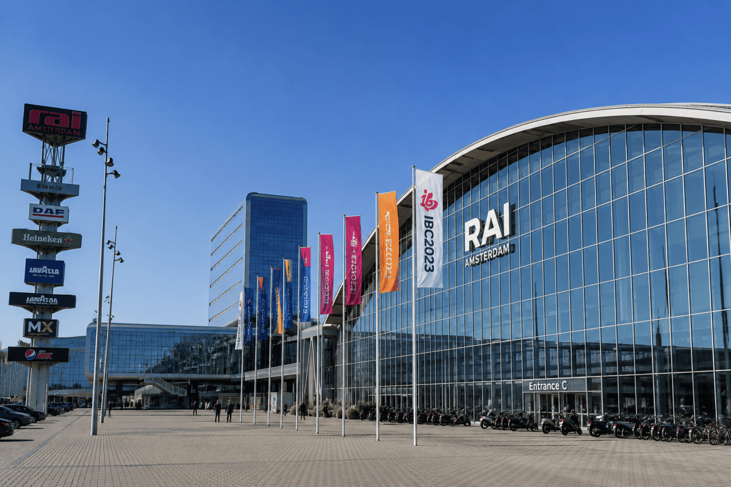 Exterior view of RAI Amsterdam during IBC 2026 with colorful flags and clear blue sky, showcasing the venue's modern architecture for media and entertainment industry event.