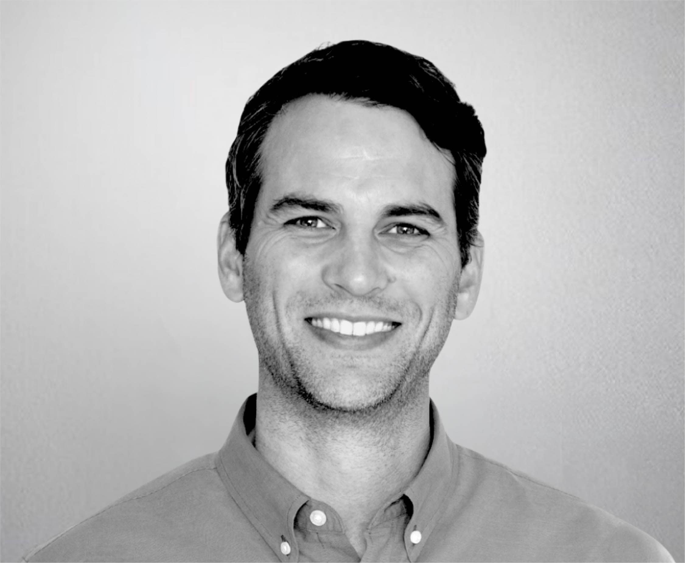 Black and white portrait of Jeff Varnell smiling, wearing a collared shirt, with a plain background.